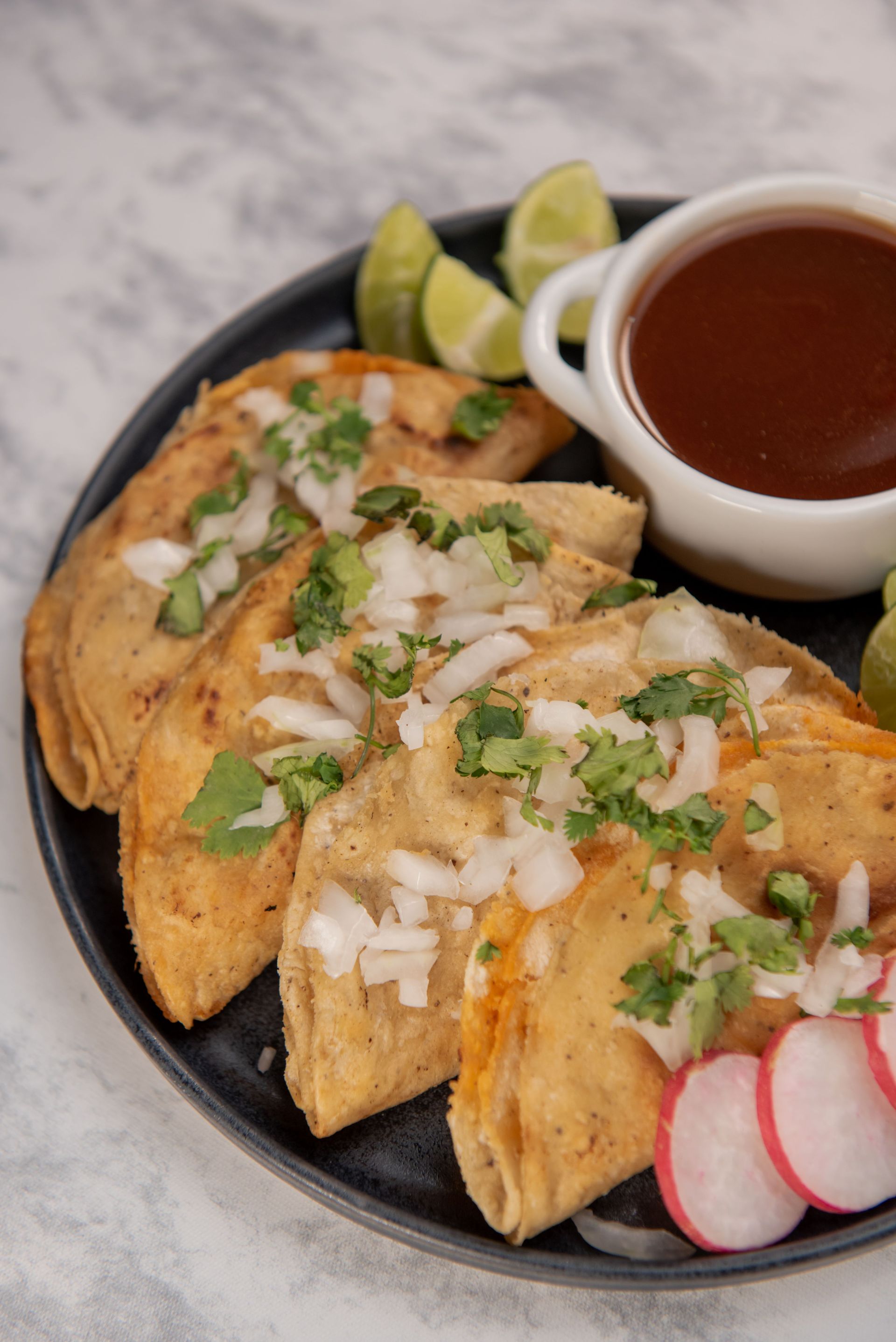 Plate of traditional Mexican street tacos garnished with onions, cilantro, and lime.